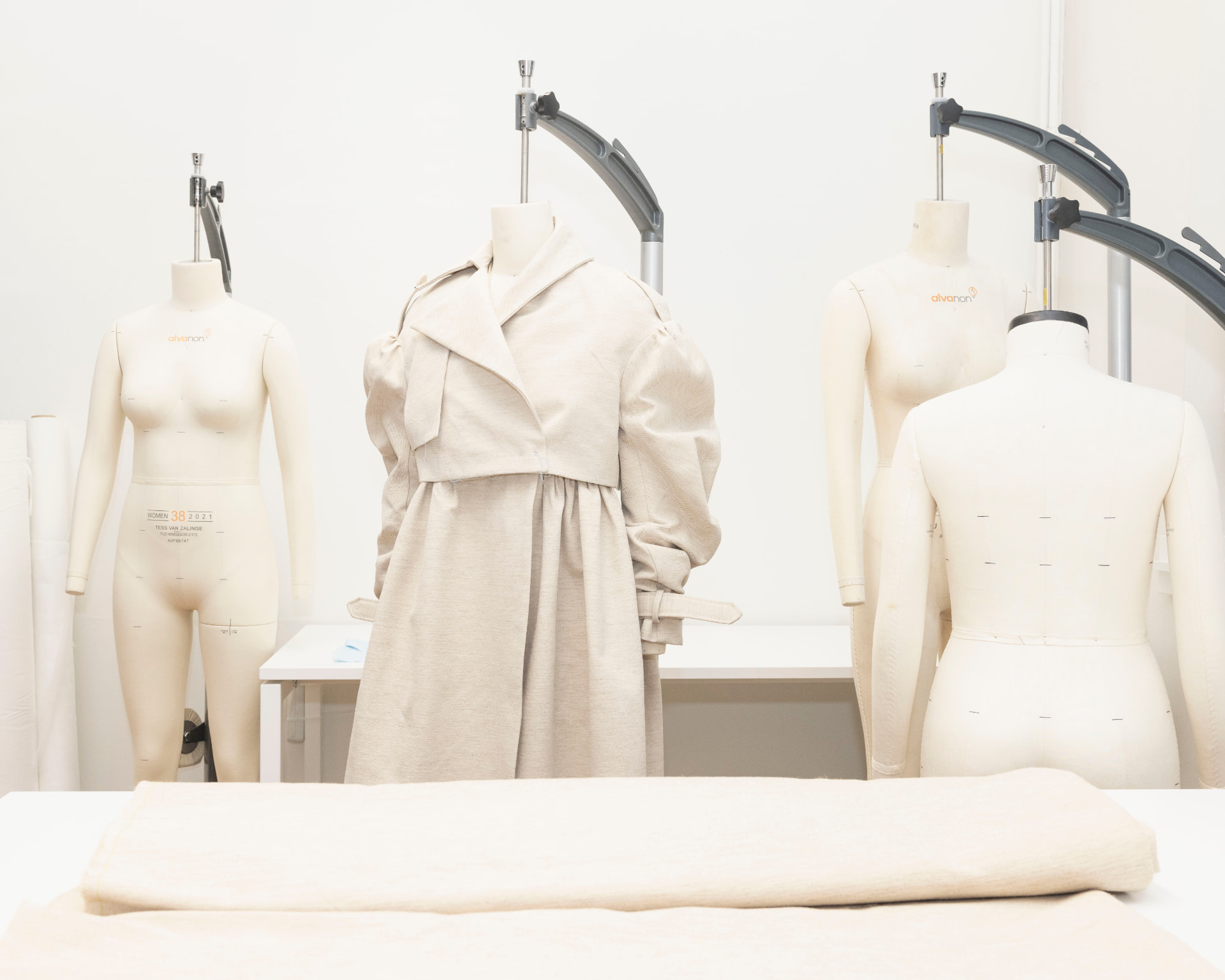 Garment prototype on a dress form beside a folded roll of keratin textile in the atelier