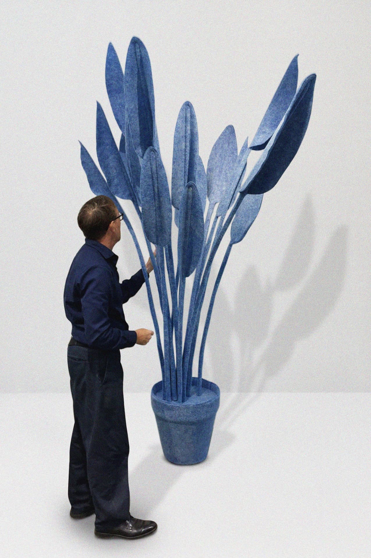 Tall ādara® Felt plant sculpture in a pot, with a person gesturing toward its leaves
